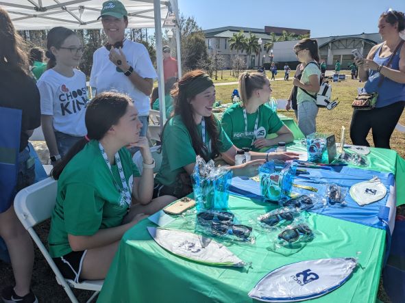 ROCK team members and volunteers stand and sit by a table at FGCU Day
